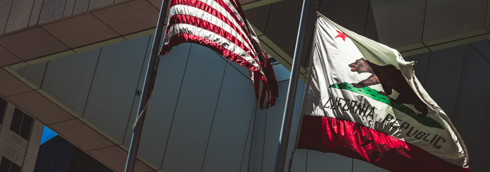 American flag and California Republic flag flying before building