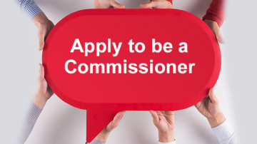 Hands holding sign that reads: "Apply to be a Commissioner"
